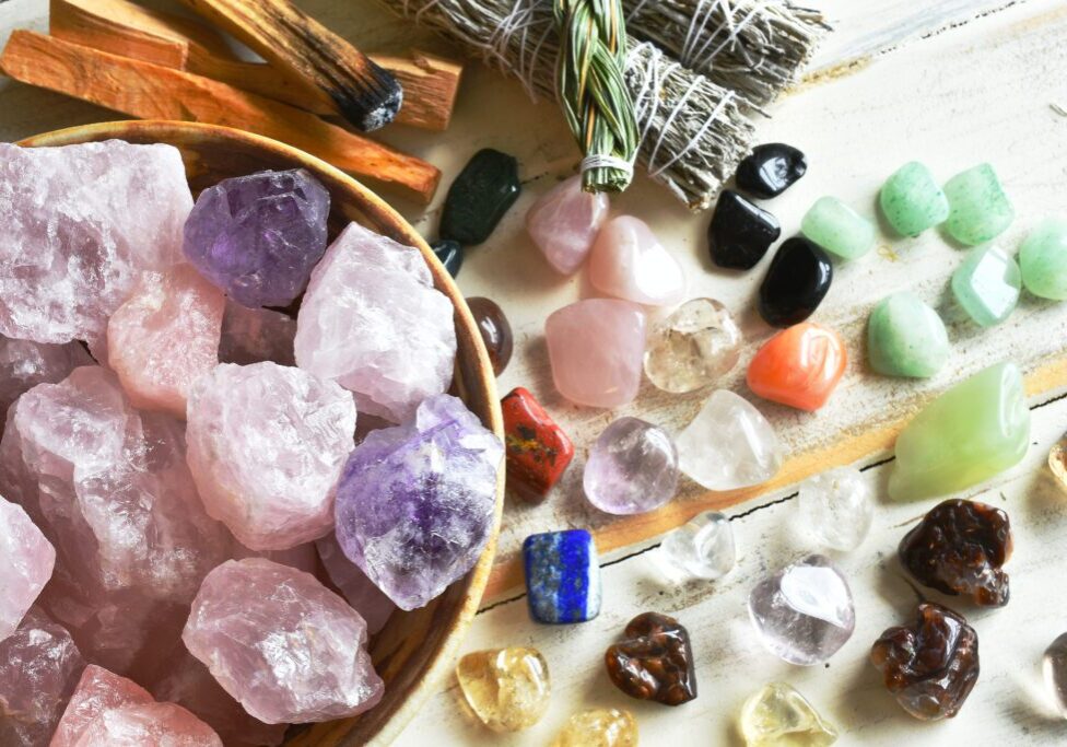 A top view image of a bowl of rose quartz crystals with several other healing crystal and smudge sticks.